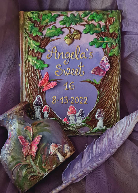 A purple guest book with a fairy forest and butterfly theme, featuring mushrooms, a feather pen, and some decorative elements on a white surface.