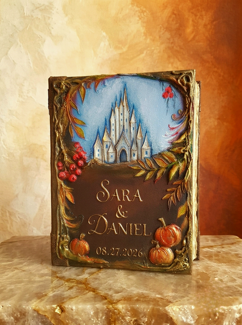 Personalized handmade hardcover Autumn wedding guest book The cover features a painted blue sky with a 3D white castle, autumn leaves, red berries, and small pumpkins, with the names 'SARA & DANIEL' and the date