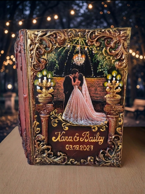 A custom, ornate hardcover wedding keepsake book standing upright on a wooden table. The book features intricate gold and brown baroque-style scrollwork borders, a central illustration of a bride and groom under a chandelier, and personalized gold text reading 'Kara & Bailey 03.