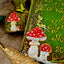 A close-up of a hand-painted decorative sign featuring red and white mushrooms, a fairy, and gold script text on a green background, styled with burlap and a gold feather.