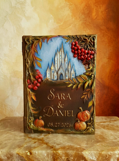 Personalized handmade hardcover Autumn wedding guest book  The cover features a painted blue sky with a 3D white castle, autumn leaves, red berries, and small pumpkins, with the names 'SARA & DANIEL' and the date