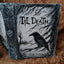 A gothic-style hardcover journal or notebook with a raven illustration and the text 'Til Death' on the cover, photographed on a brown textured fabric background.