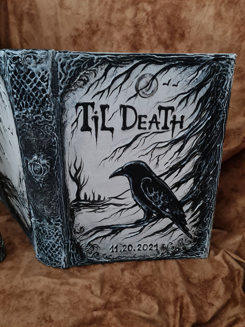 A gothic-style hardcover journal or notebook with a raven illustration and the text 'Til Death' on the cover, photographed on a brown textured fabric background.