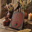 A rustic decorative sign reading 'Be Our Guest' in raised lettering, styled on a wooden table with dried flowers, small vases, a candle, and a gold feather quill in a warm, rustic setting.