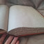 An open vintage book with blank, aged beige paper pages and a worn reddish-brown leather or cloth binding, held open by a hand against a neutral fabric background.