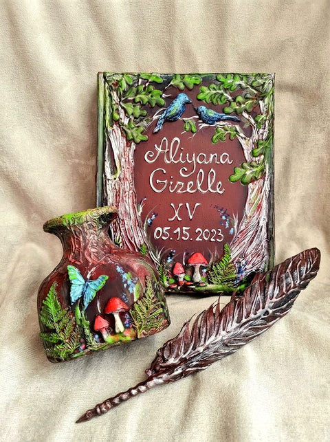 A personalized painted wooden keepsake box set displayed on a beige fabric background, featuring a rectangular box with a forest design, a matching small vase, and a decorative feather quill.